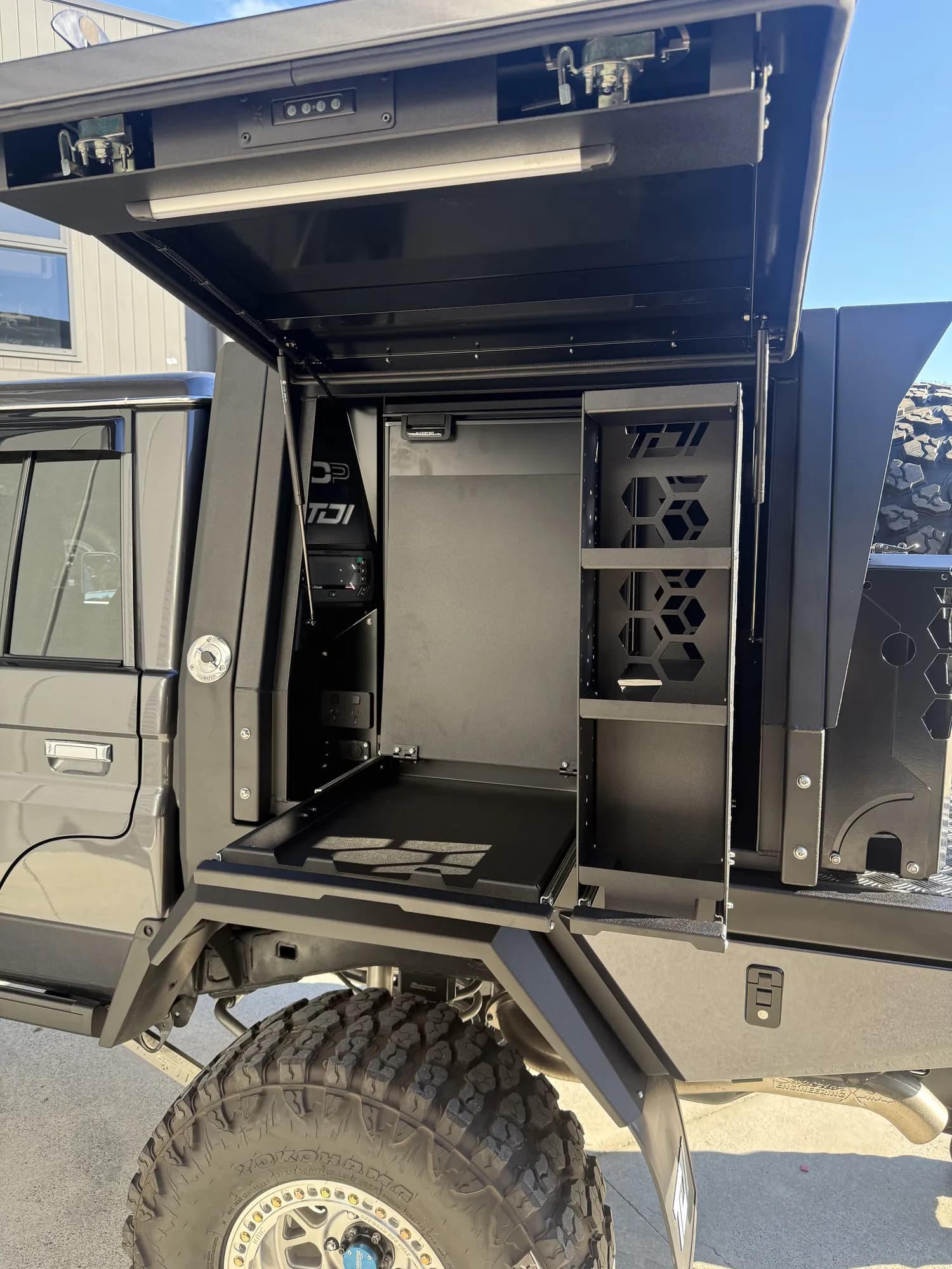 A grey 79 Series with its canopy wing raised, showing a slide-out drawer, shelving and power outlets above a large off-road tyre