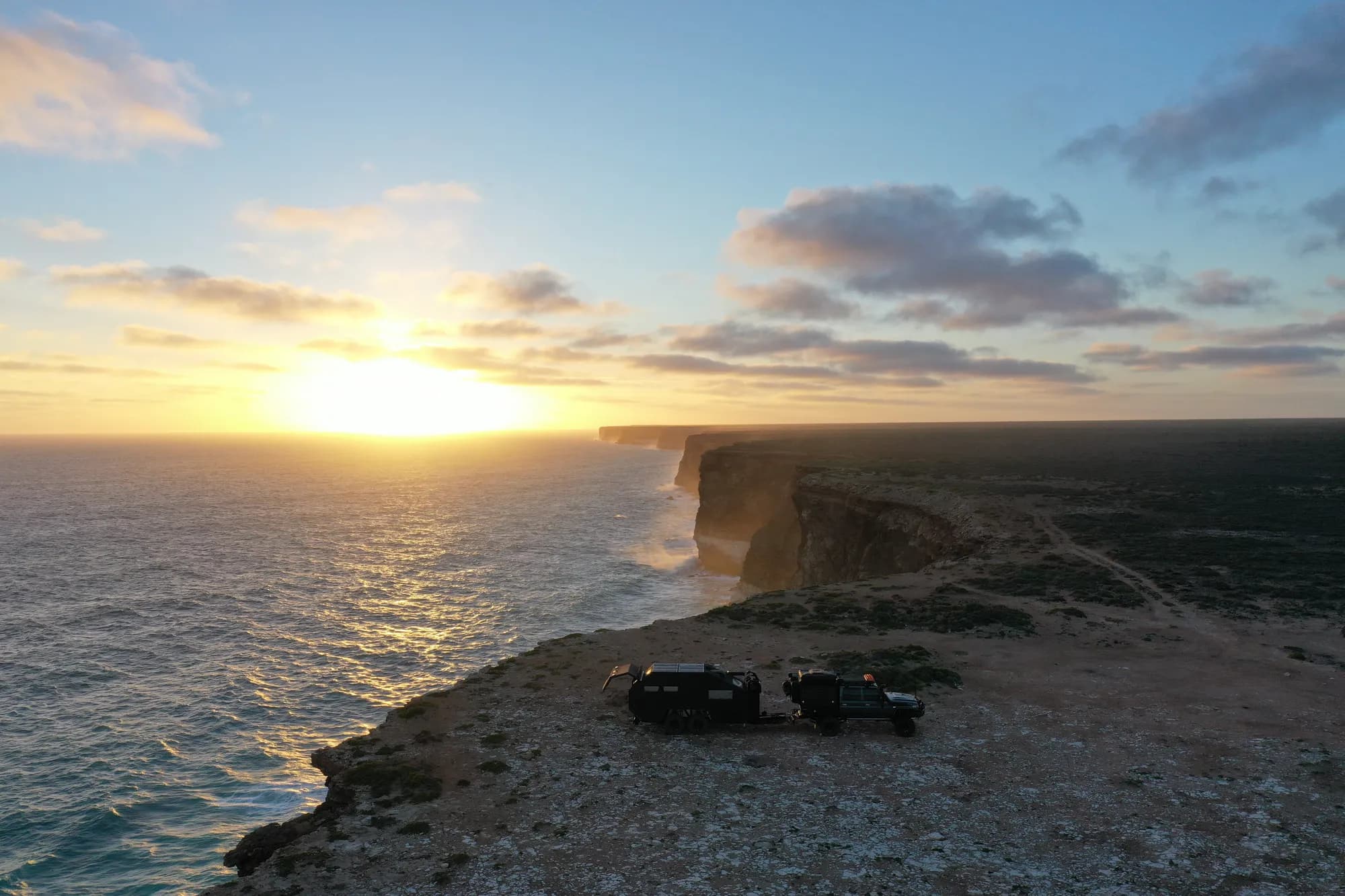 Drone view of a 4x4 and off-road caravan parked on the Nullarbor clifftops above the Great Australian Bight at sunset